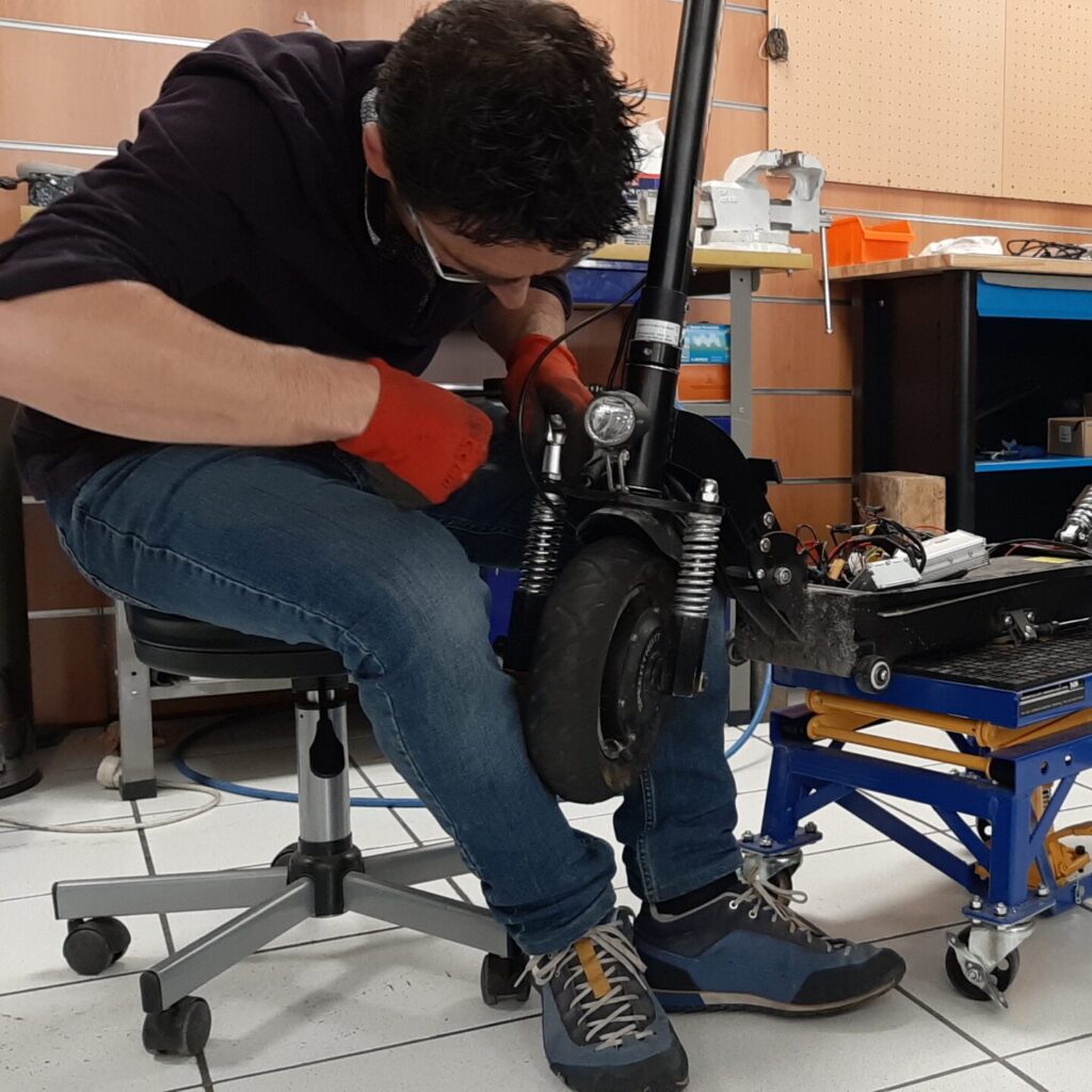 Le jeune homme fait la vérification des amortisseurs d'une trottinette électrique dans un atelier Citytrott