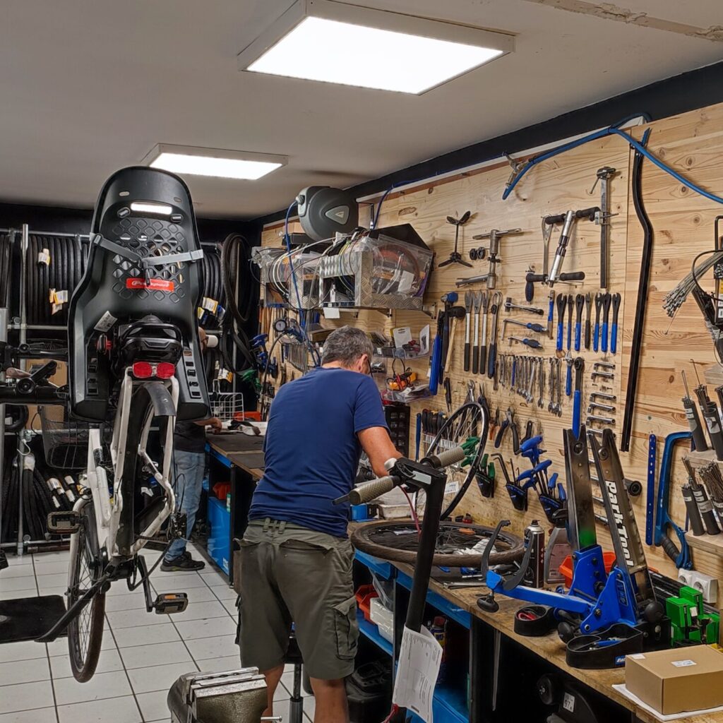 Dans un atelier Citytrott , révision d'un vélo électrique équipé de son siège enfant. L'homme vérifie la roue arrière du vélo électrique.