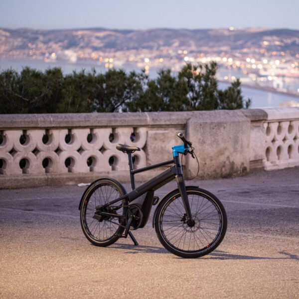 Un vélo électrique I-WEECH noir et bleu sur un balcon en pierre devant la mer