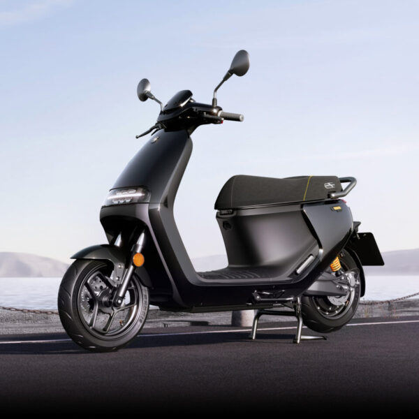 Scooter noir électrique sur sa béquille vu de profil devant un lac