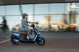 Une femme élégante en talon et avec un casque se déplace à scooter électrique