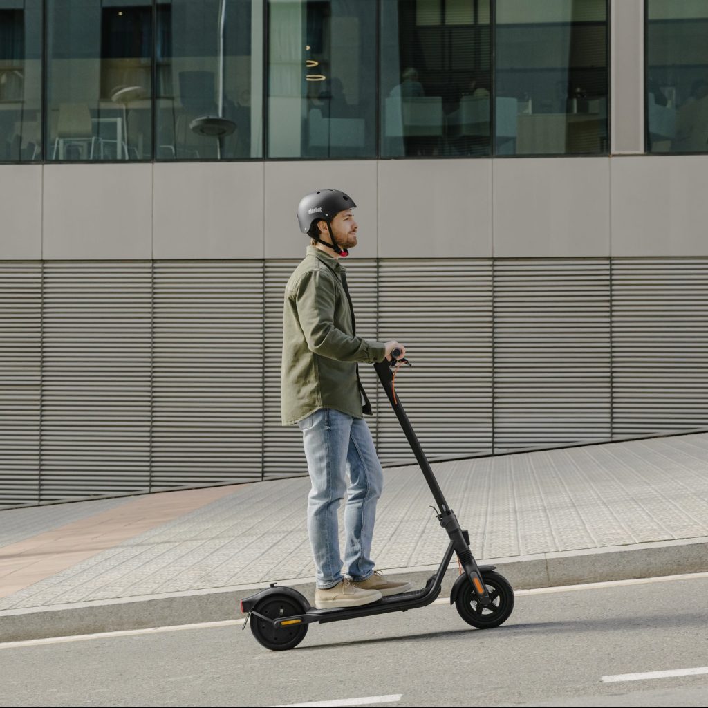 Segway Ninebot F2-Pro trottinette électrique un homme se rend au travaille avec un casque et des immeubles derrière