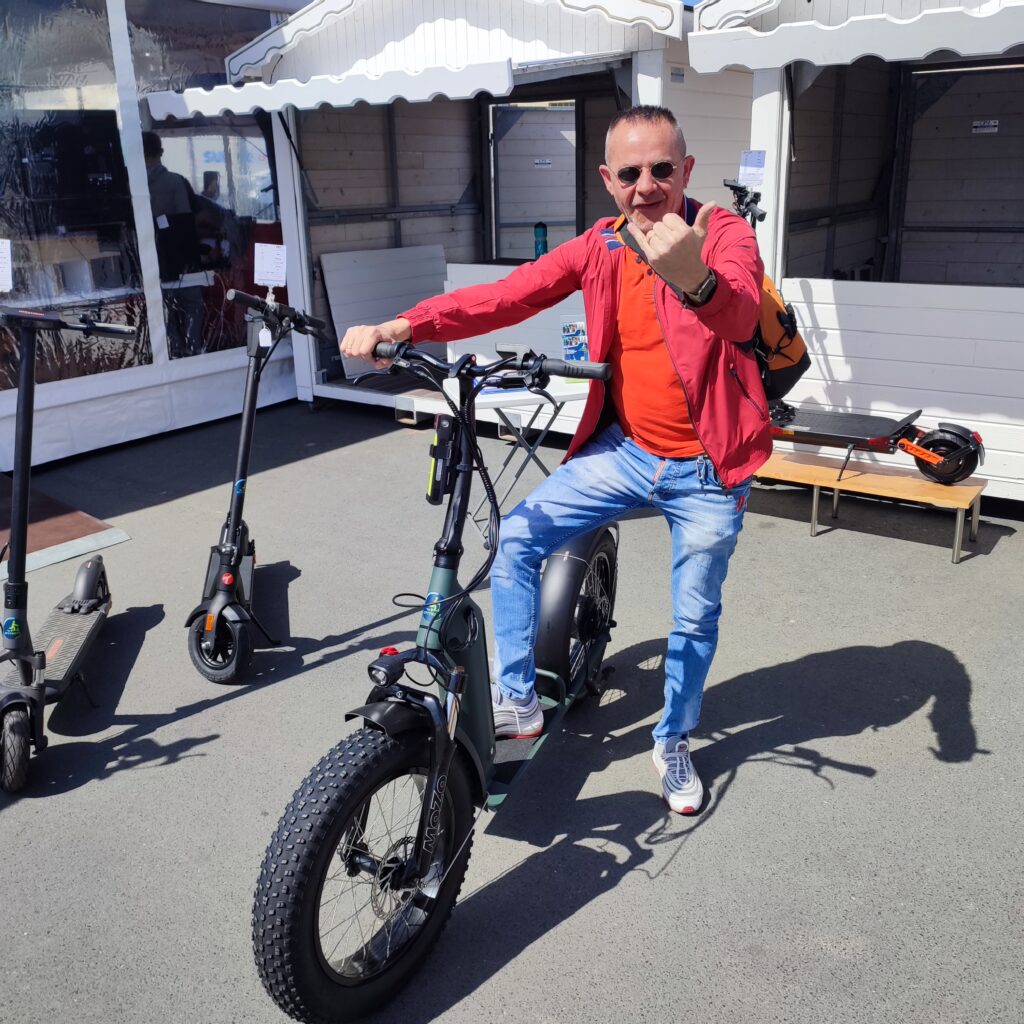 Un homme avec le pouce levé essaye une trottinette électrique avec des grosses roues au magasin Citytrott