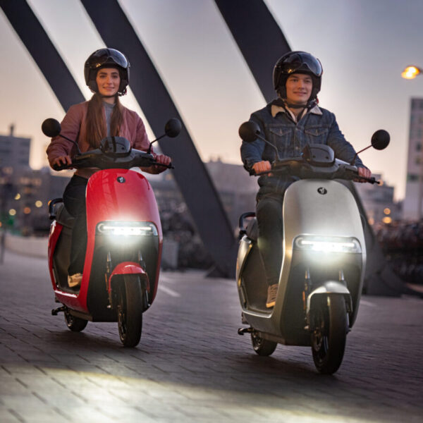 jeune fille sur un scooter électrique rouge et son ami sur un scooter électrique gris tout les deux portent une casque noir visière intégrée