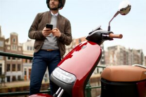 Le scooter électrique Segway en coloris rouge avec selle beige se tient à côté d'un homme qui le démarre avec son application mobile